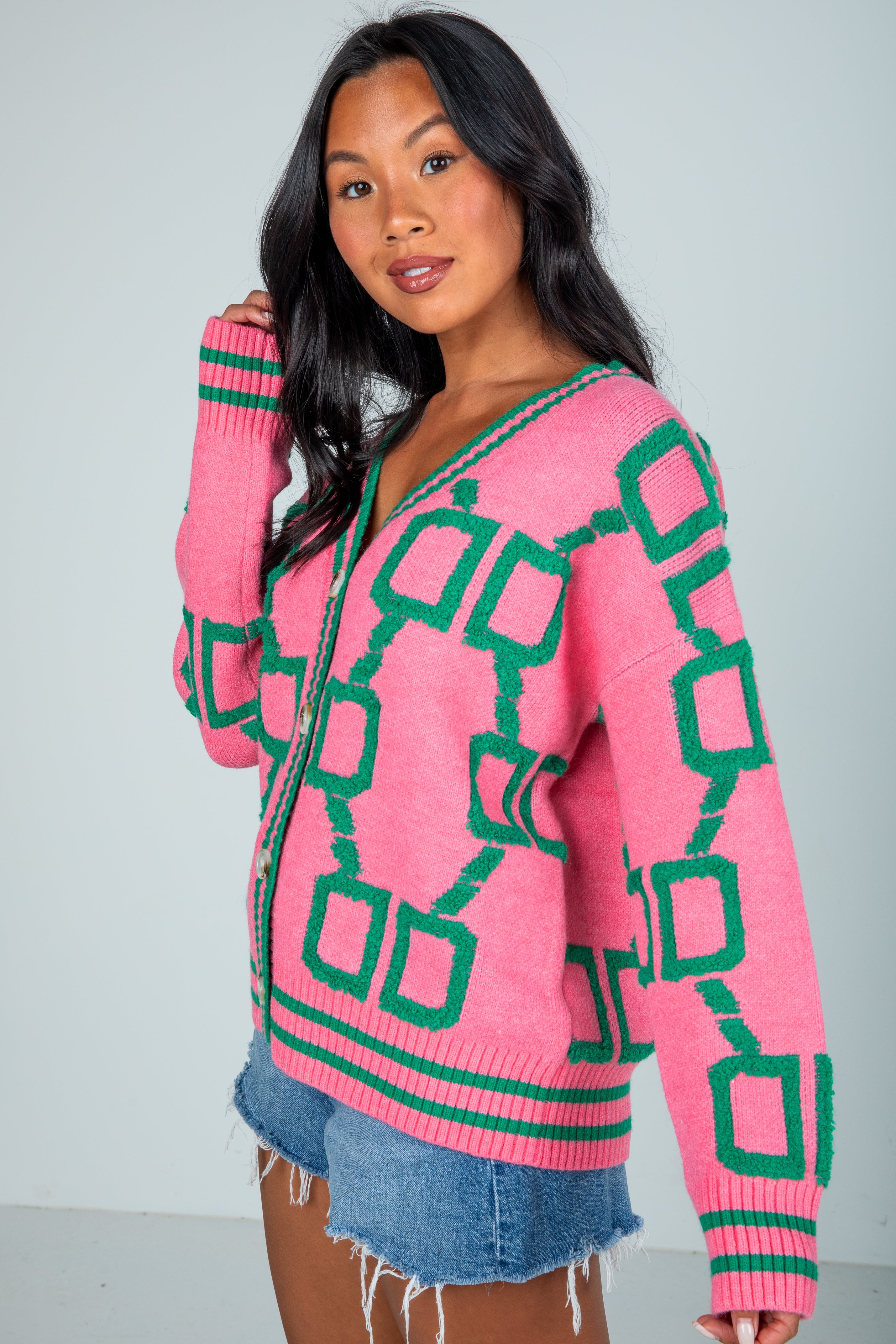 Woman wearing a pink sweater with green geometric patterns on a plain background
