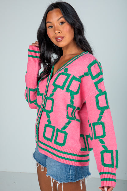 Woman wearing a pink sweater with green geometric patterns on a plain background