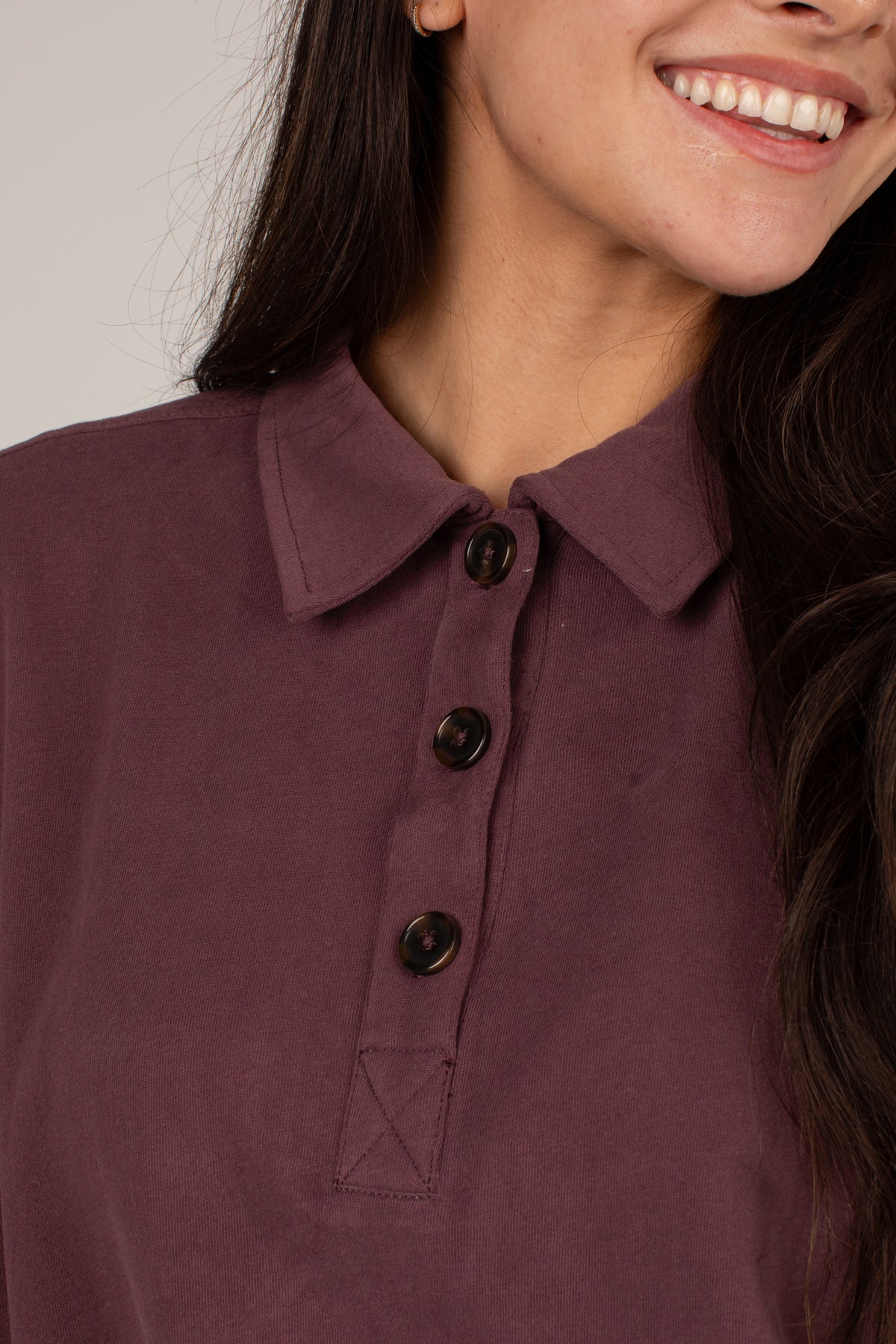 Close-up of a woman wearing a dusty plum purple polo shirt with three dark buttons and a pointed collar.