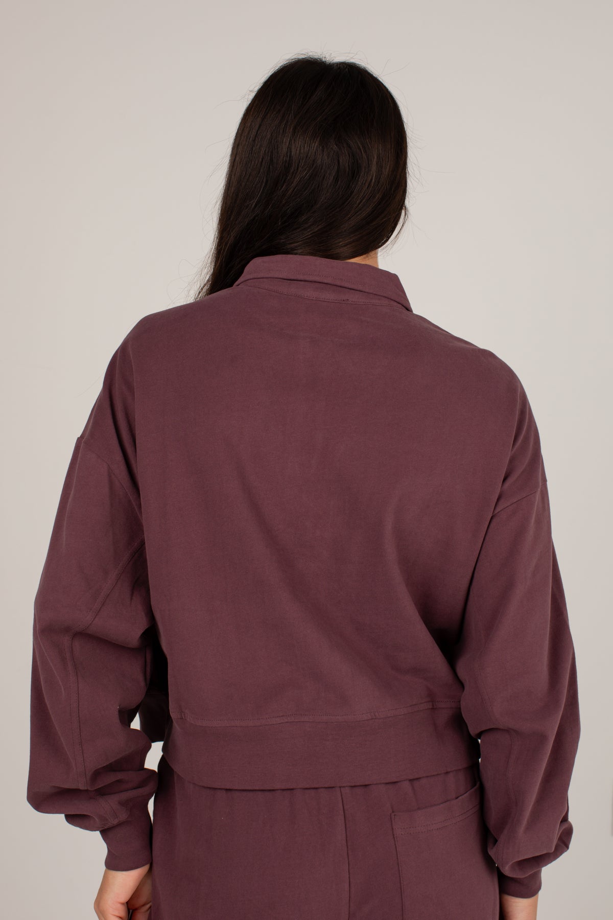 A person shown from the back wearing a matching mauve-brown corduroy jacket and pants set against a plain light gray studio background.