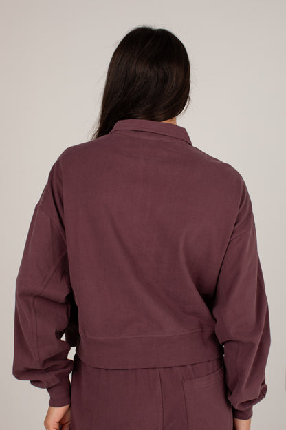 A person shown from the back wearing a matching mauve-brown corduroy jacket and pants set against a plain light gray studio background.