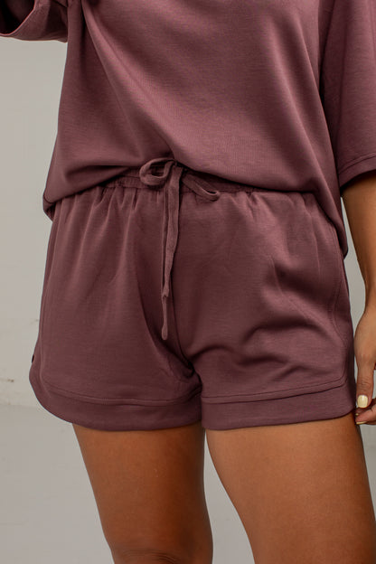 A close-up of a person wearing a matching lounge set in a dusty mauve color, featuring a short-sleeve top and drawstring shorts.