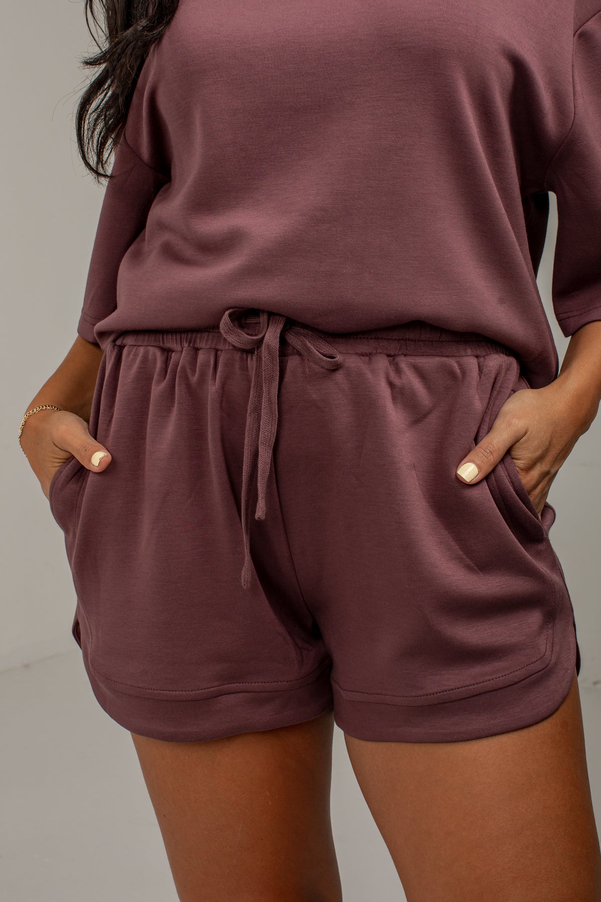 A person wearing a matching lounge set in a dusty mauve-brown color, featuring a long-sleeve top and drawstring shorts with side pockets.