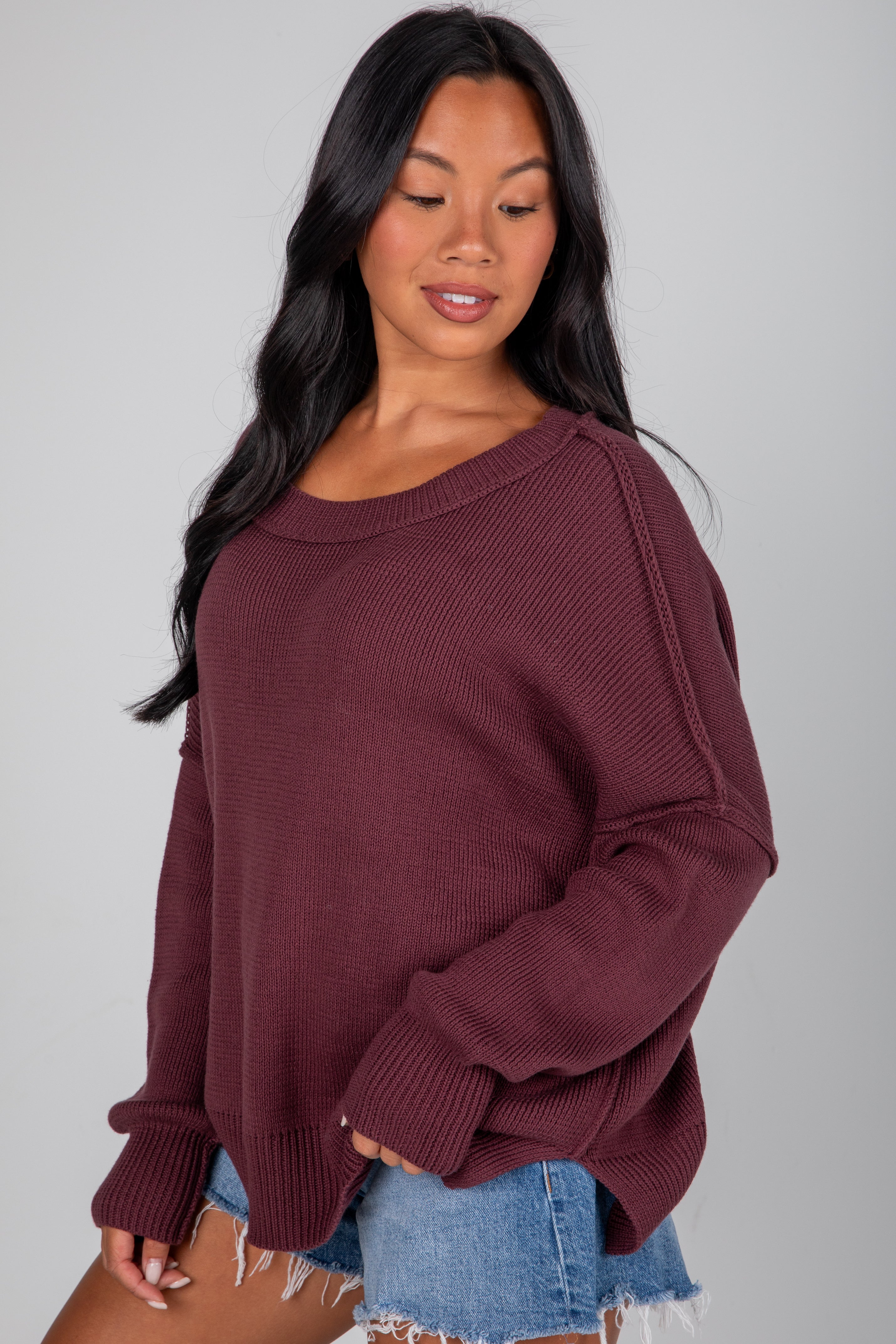 Woman wearing a maroon sweater and denim shorts on a gray background