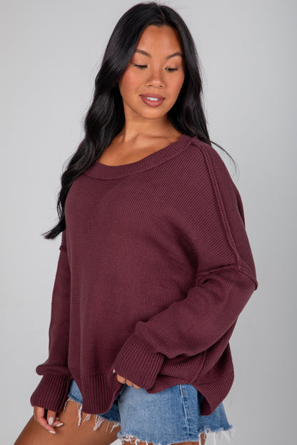 Woman wearing a maroon sweater and denim shorts on a gray background