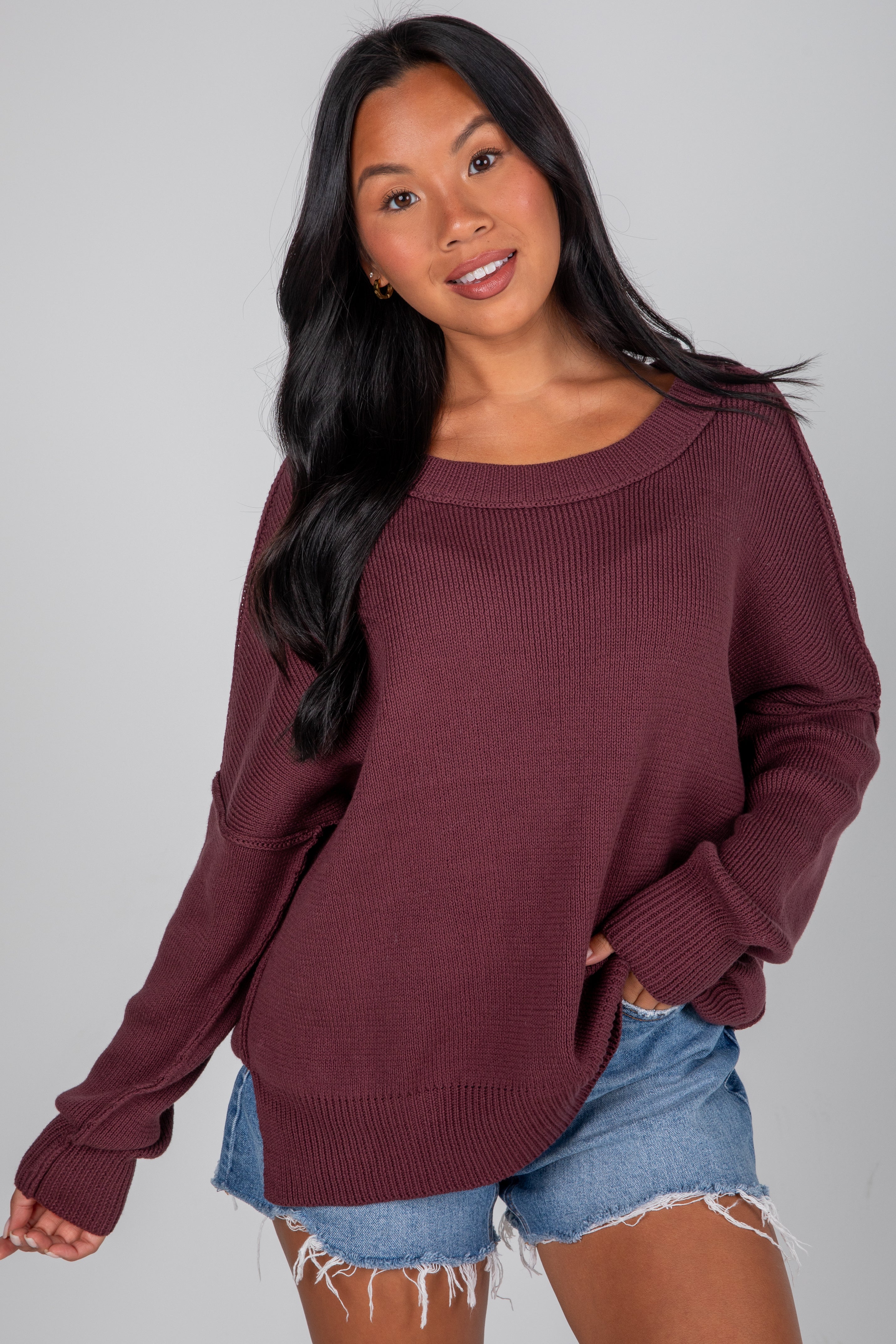 Woman wearing a burgundy sweater and denim shorts on a gray background