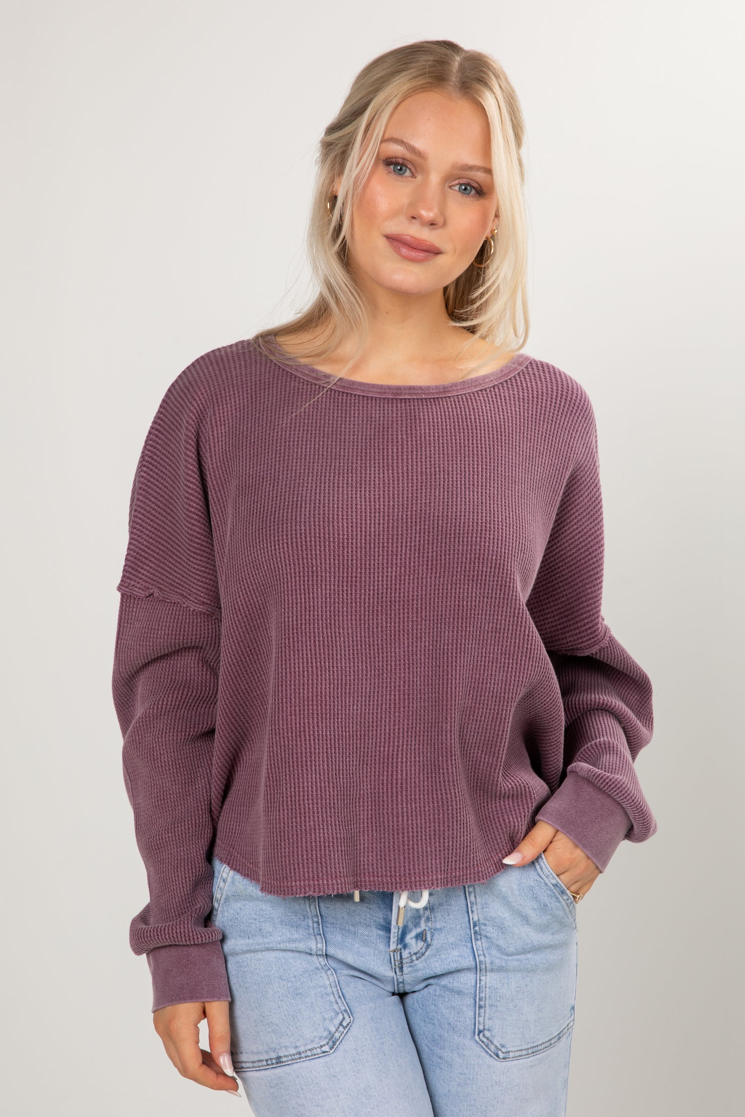 Woman wearing a purple sweater and light blue jeans against a plain background