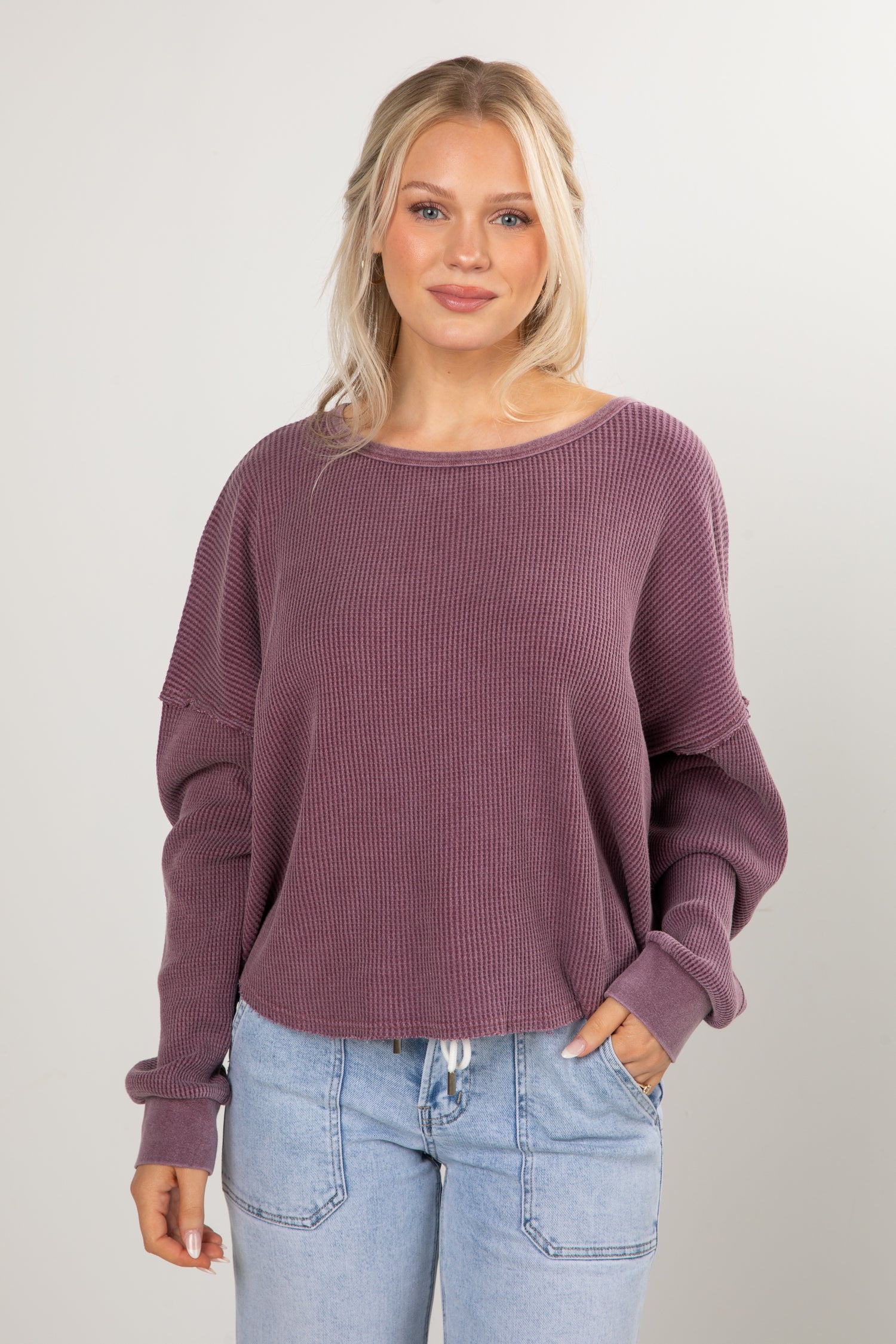 Woman wearing a purple sweater and light blue jeans against a plain background