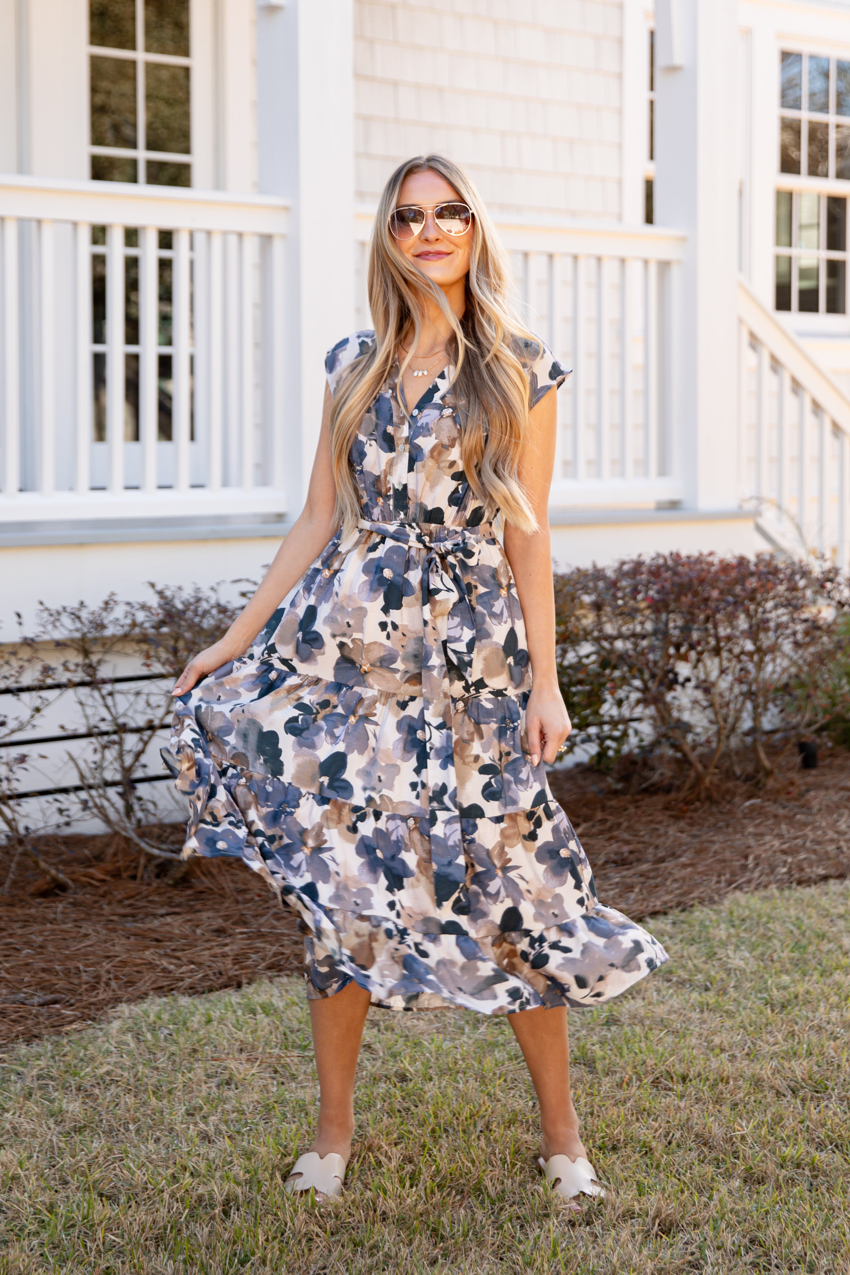 Woman wearing a floral dress standing in front of a white house.