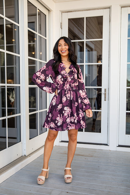 Woman in a purple floral dress standing on a wooden deck with glass doors in the background
