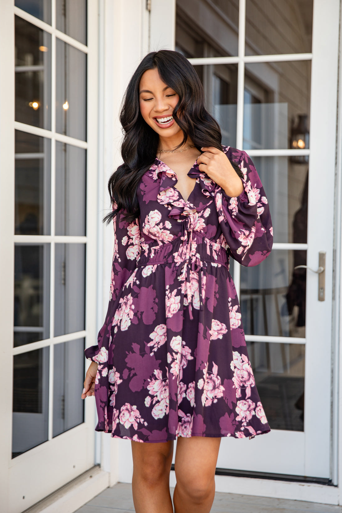 Woman wearing a purple floral dress standing in front of a glass door.