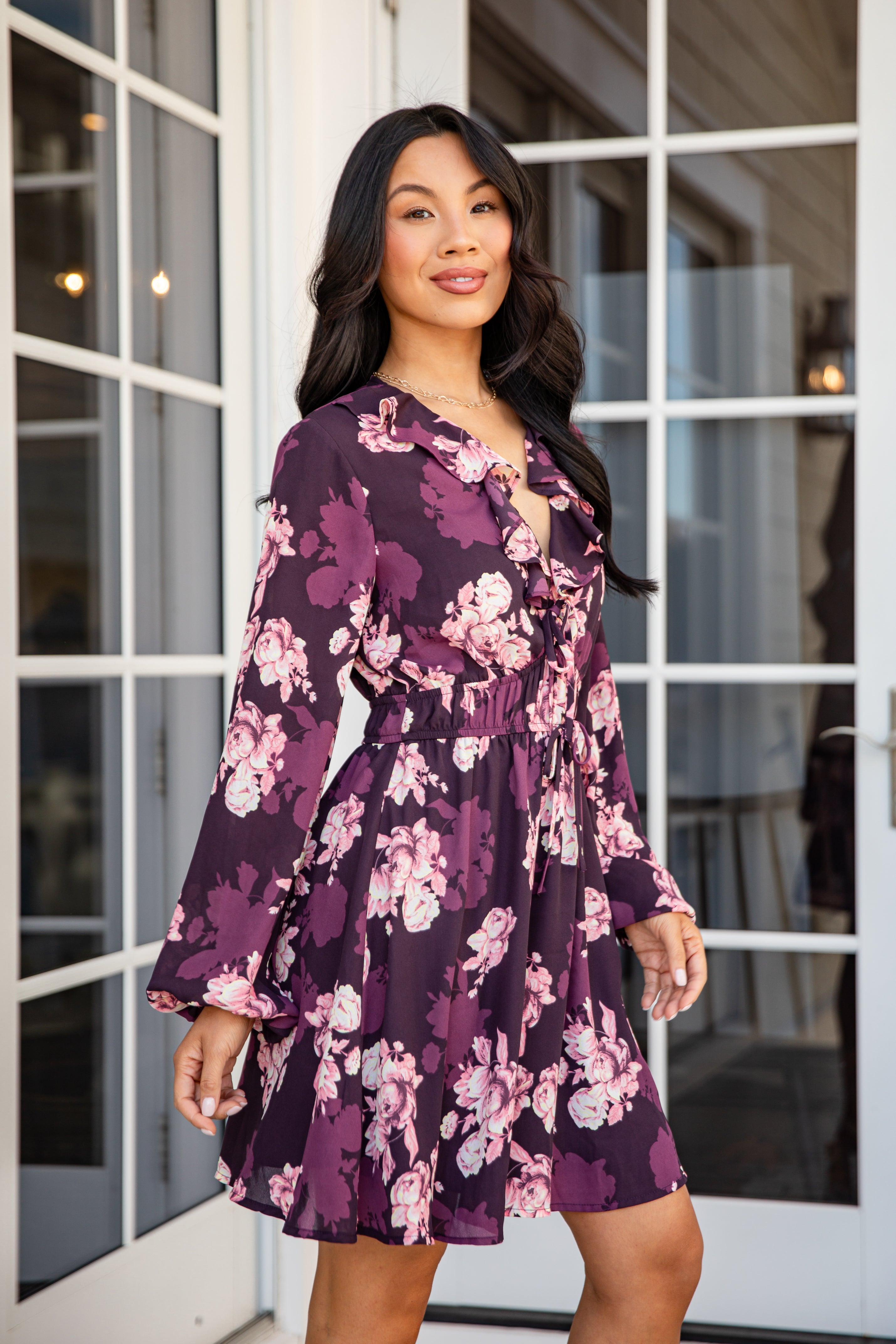 Woman wearing a purple floral dress standing in front of glass doors.