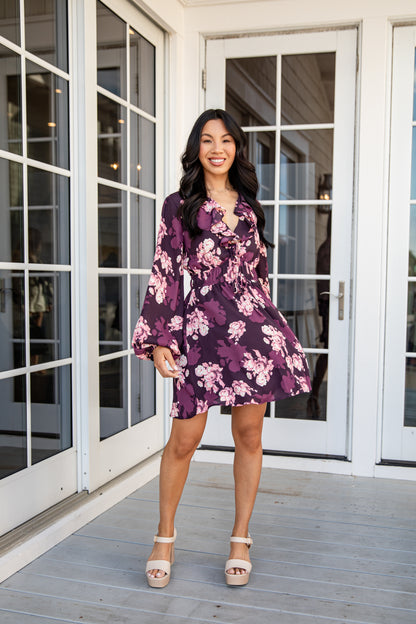 Woman in a purple floral dress standing on a wooden deck.