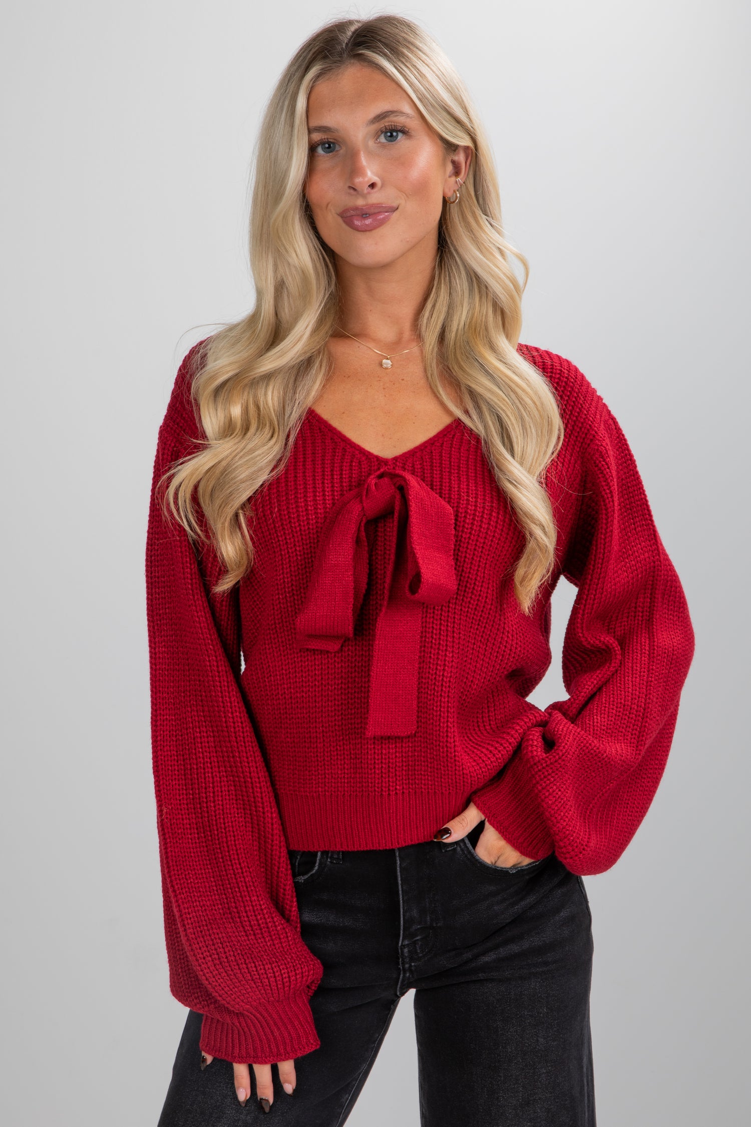 Woman wearing a red sweater with a bow detail on a gray background