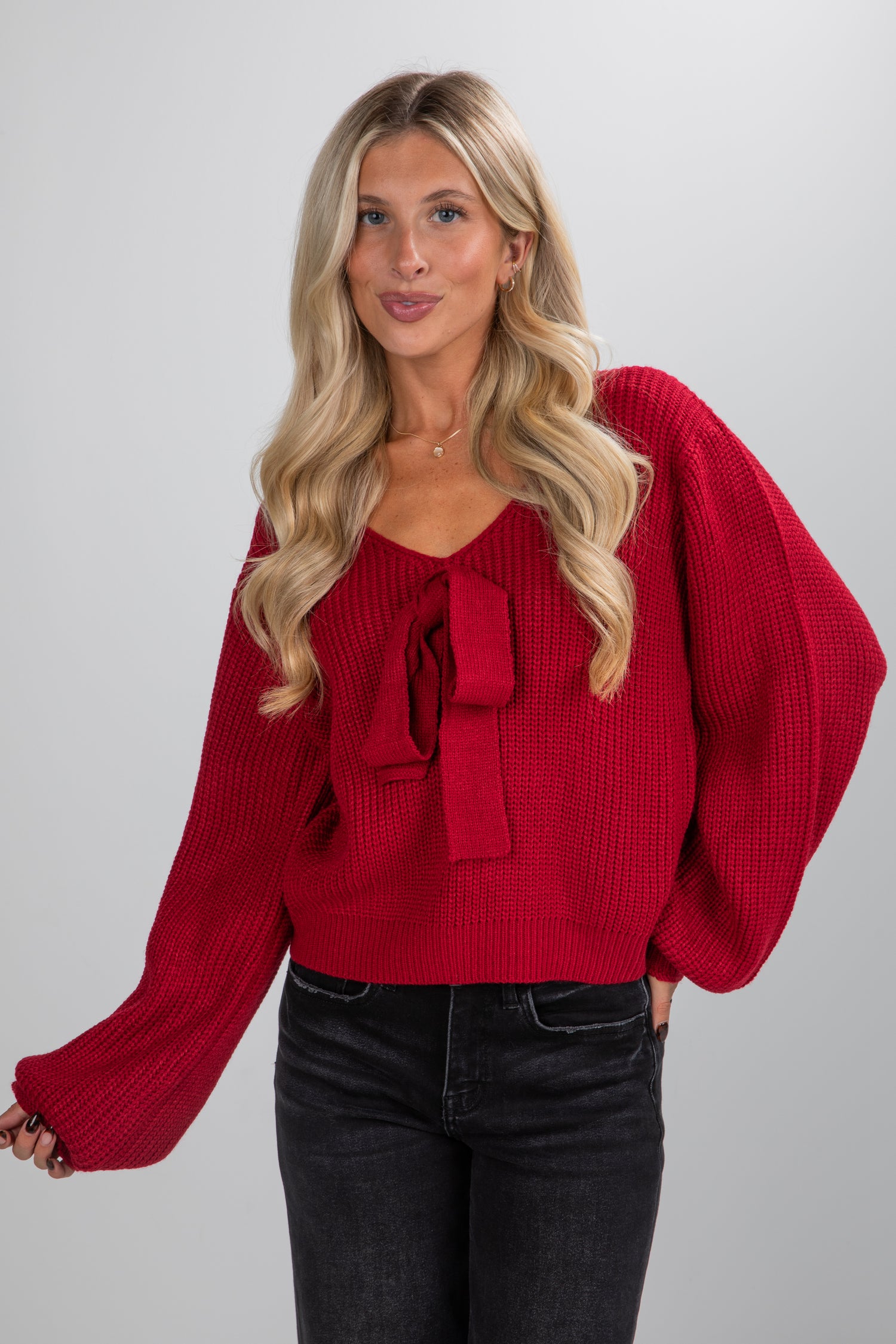 Woman wearing a red sweater with a bow detail on a plain background