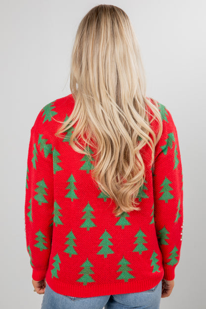 Person wearing a red sweater with green tree patterns on a plain background