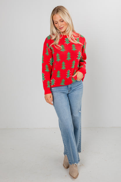 Woman wearing a red sweater with green tree patterns and blue jeans on a white background