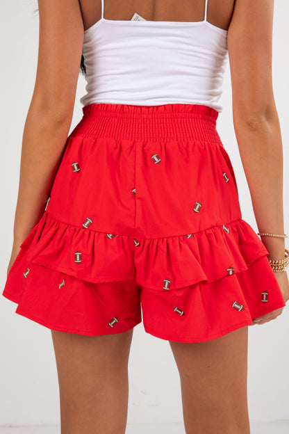 Red tiered shorts with silver embellishments worn by a person on a white background