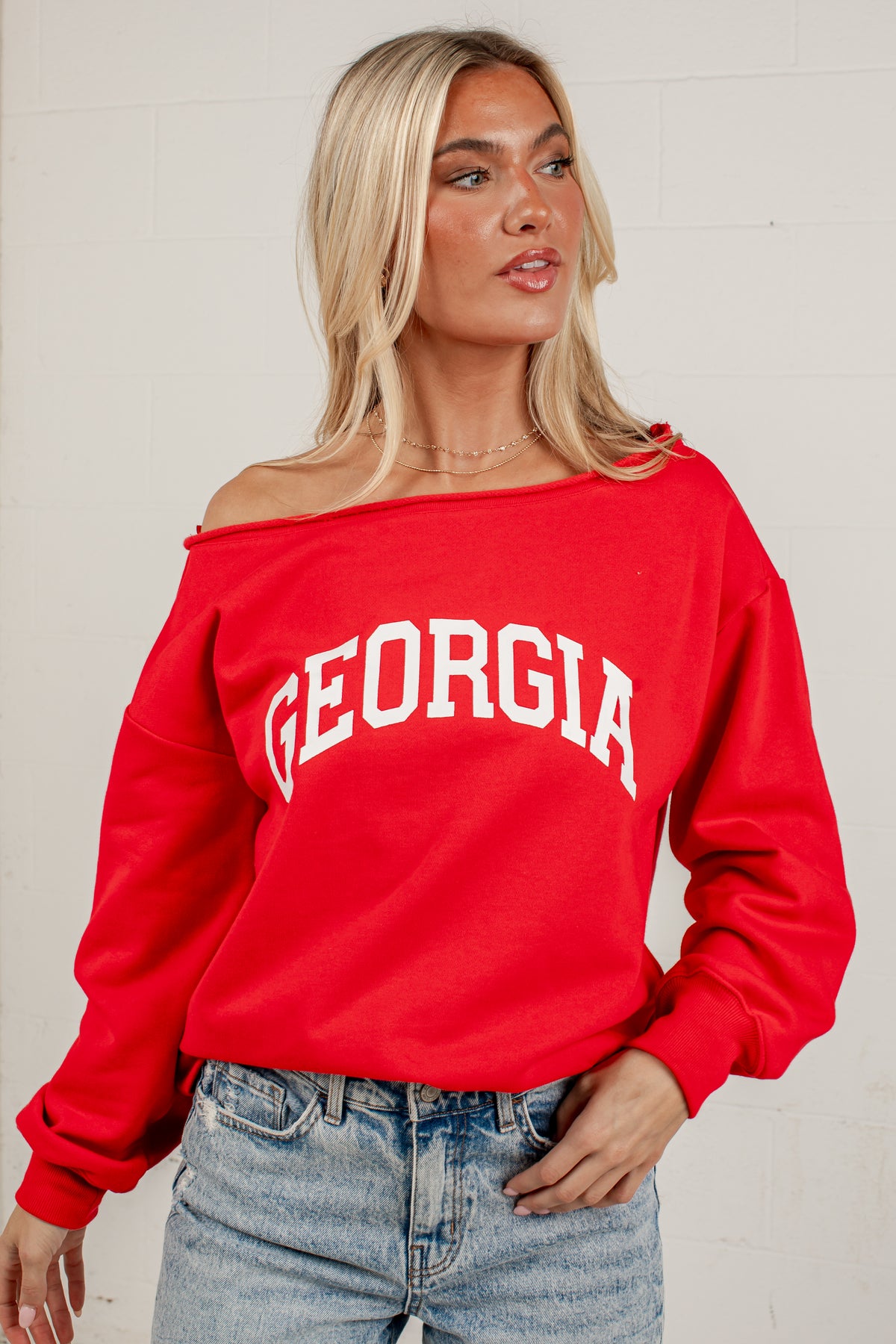 A woman wearing a bright red off-the-shoulder sweatshirt with &