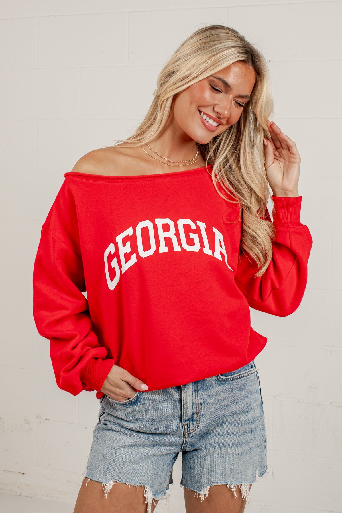 A woman wearing a bright red off-the-shoulder sweatshirt with &