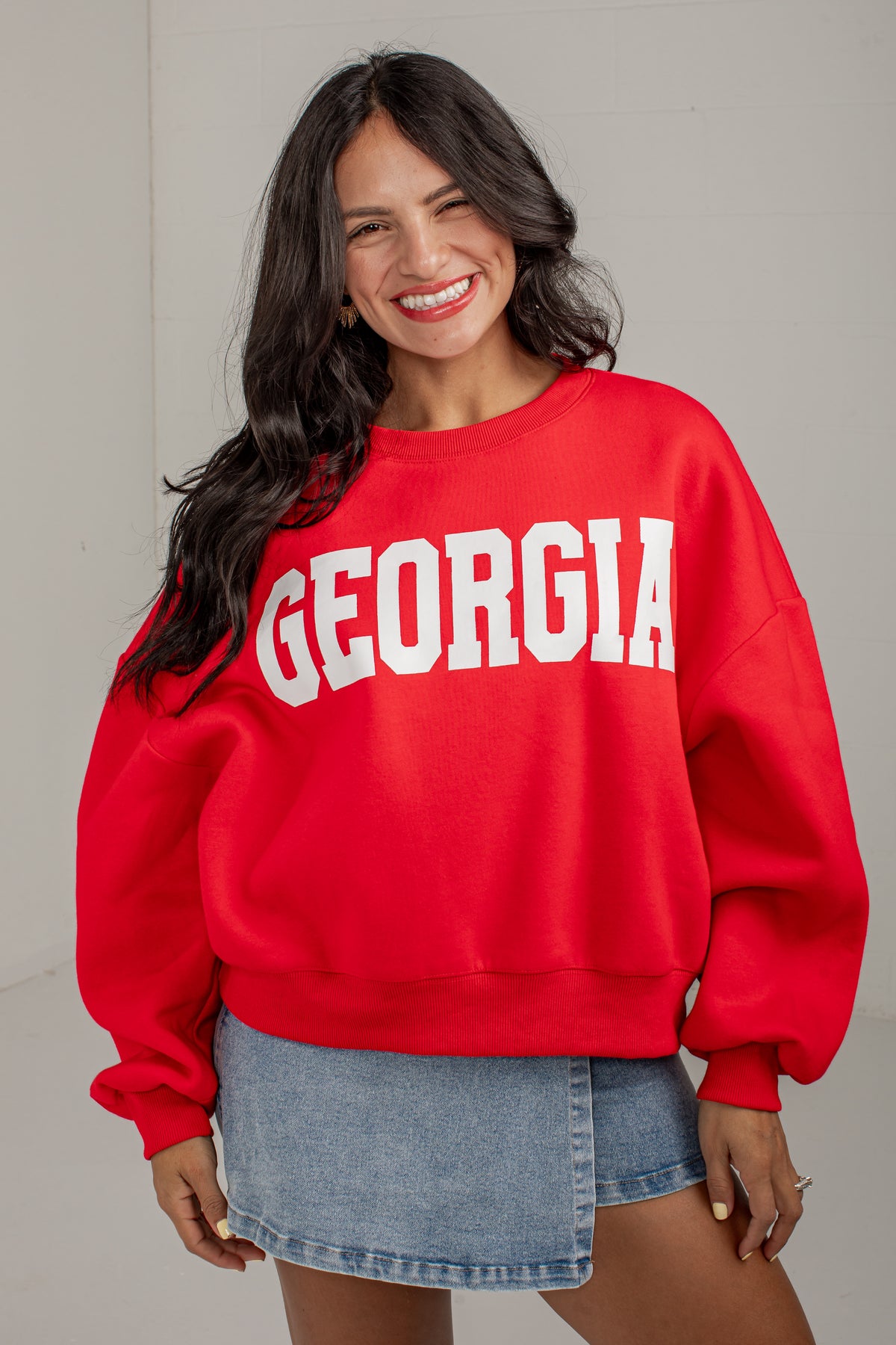 A woman smiling and wearing a bright red crewneck sweatshirt with &