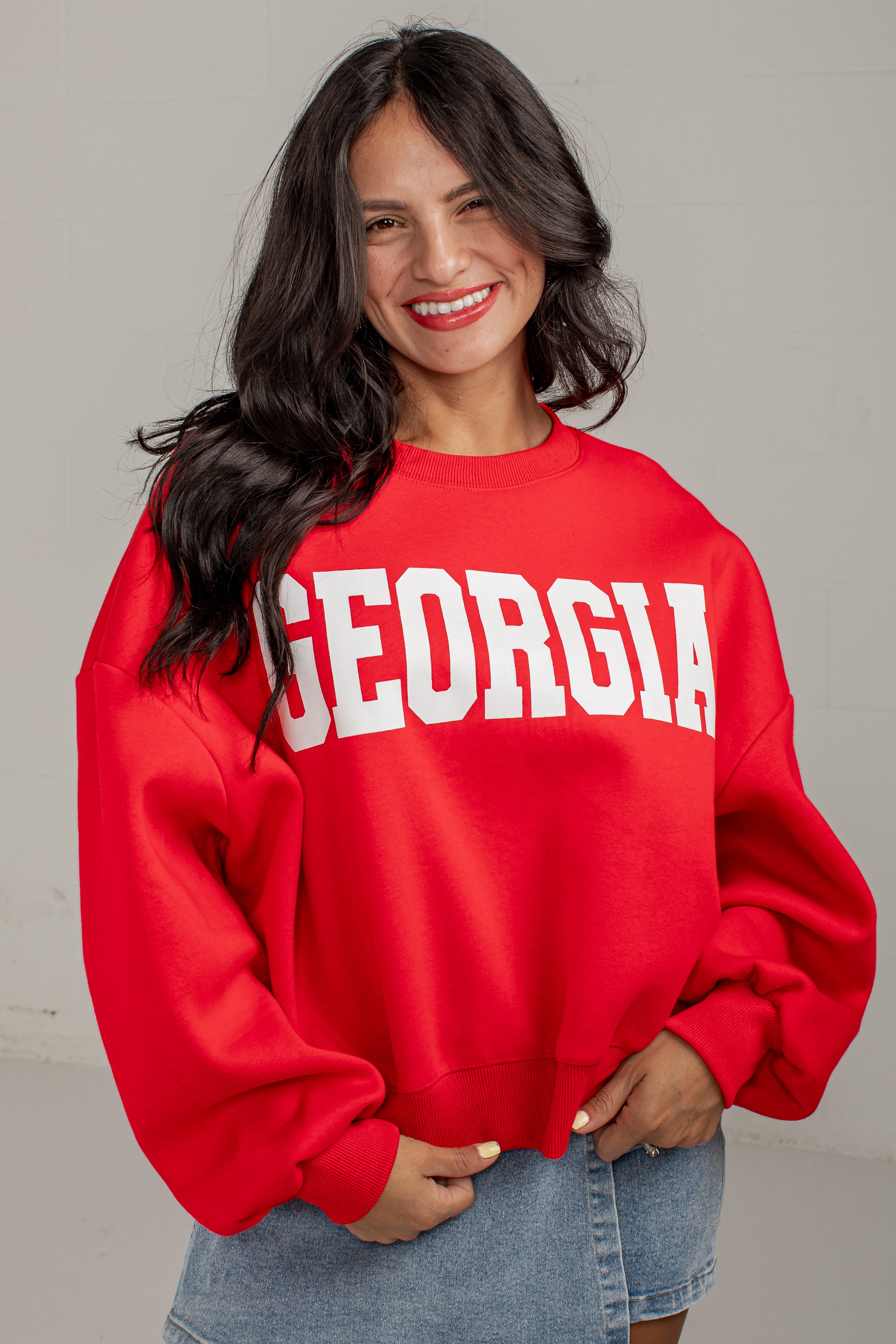 A woman wearing a bright red crewneck sweatshirt with &