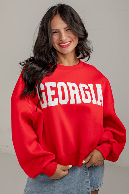 A woman wearing a bright red crewneck sweatshirt with &