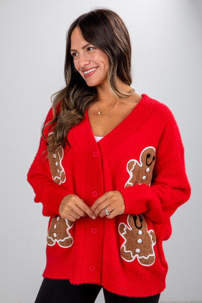 Woman wearing a red cardigan with gingerbread man designs on a plain background