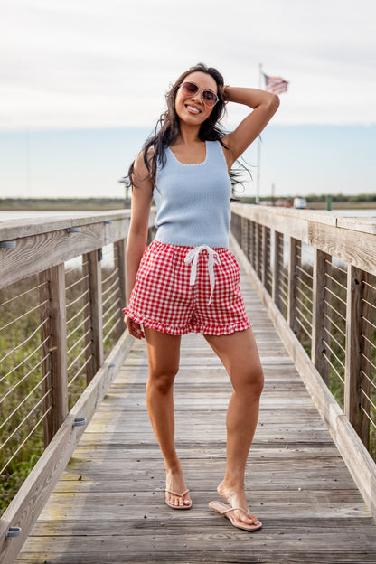 Woman in light blue tank top and red checkered shorts standing on a wooden boardwalk.