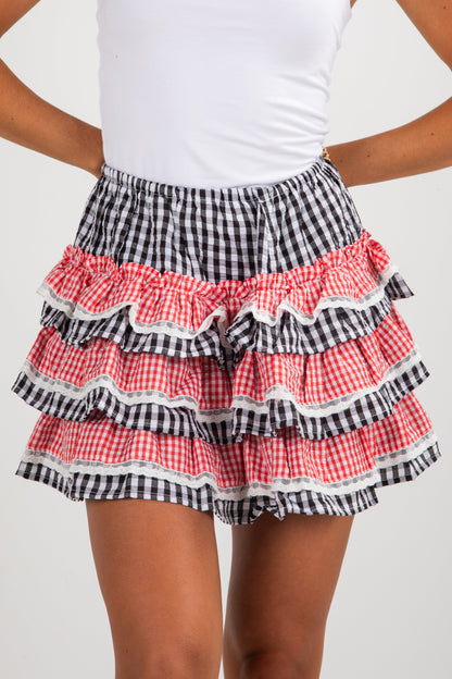 Person wearing a checkered skirt with ruffled layers on a plain background