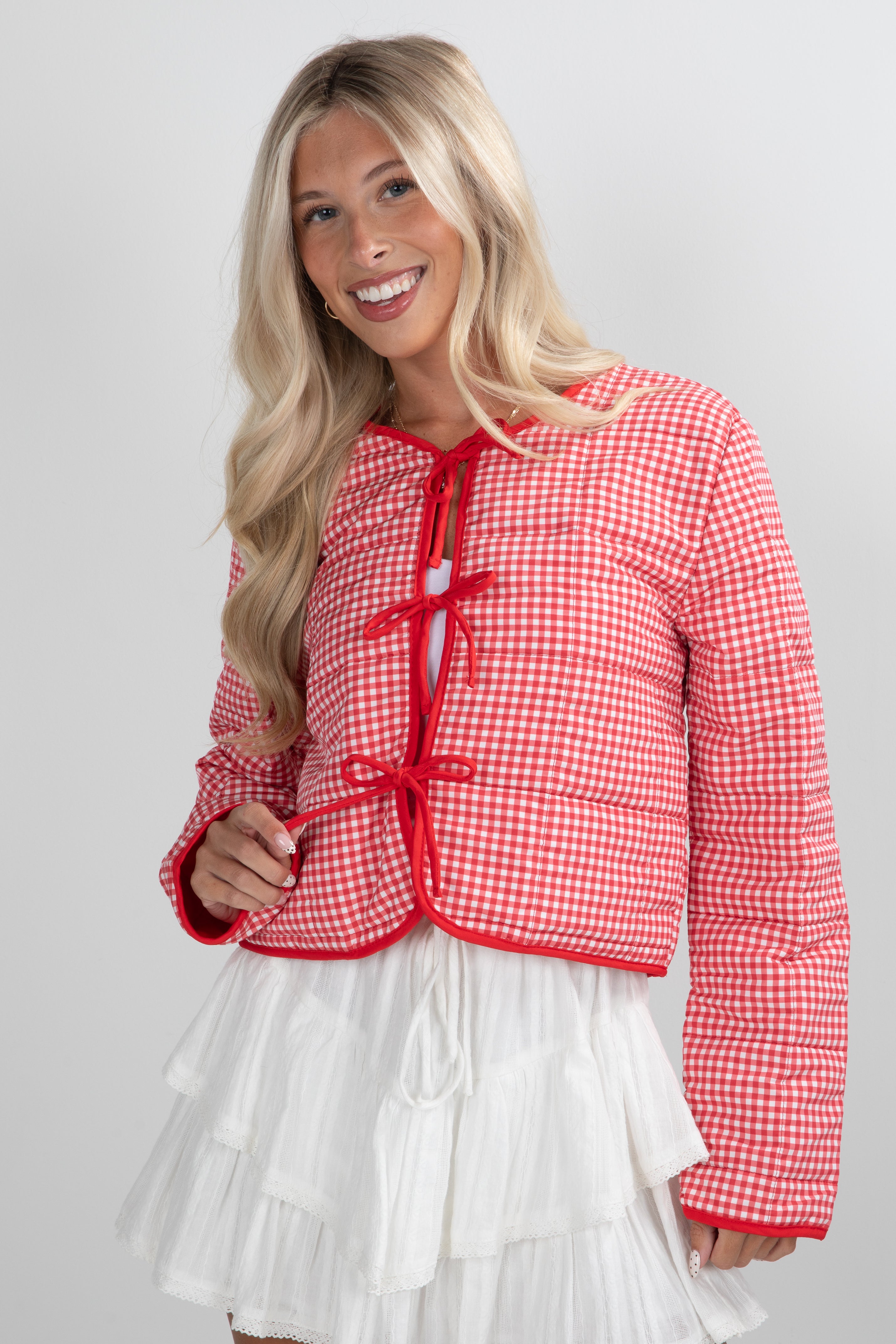 Woman wearing a red and white checkered jacket with a white skirt on a light gray background