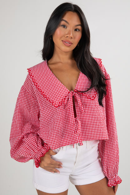 Woman wearing a red and white checkered blouse with ruffled details on a plain background