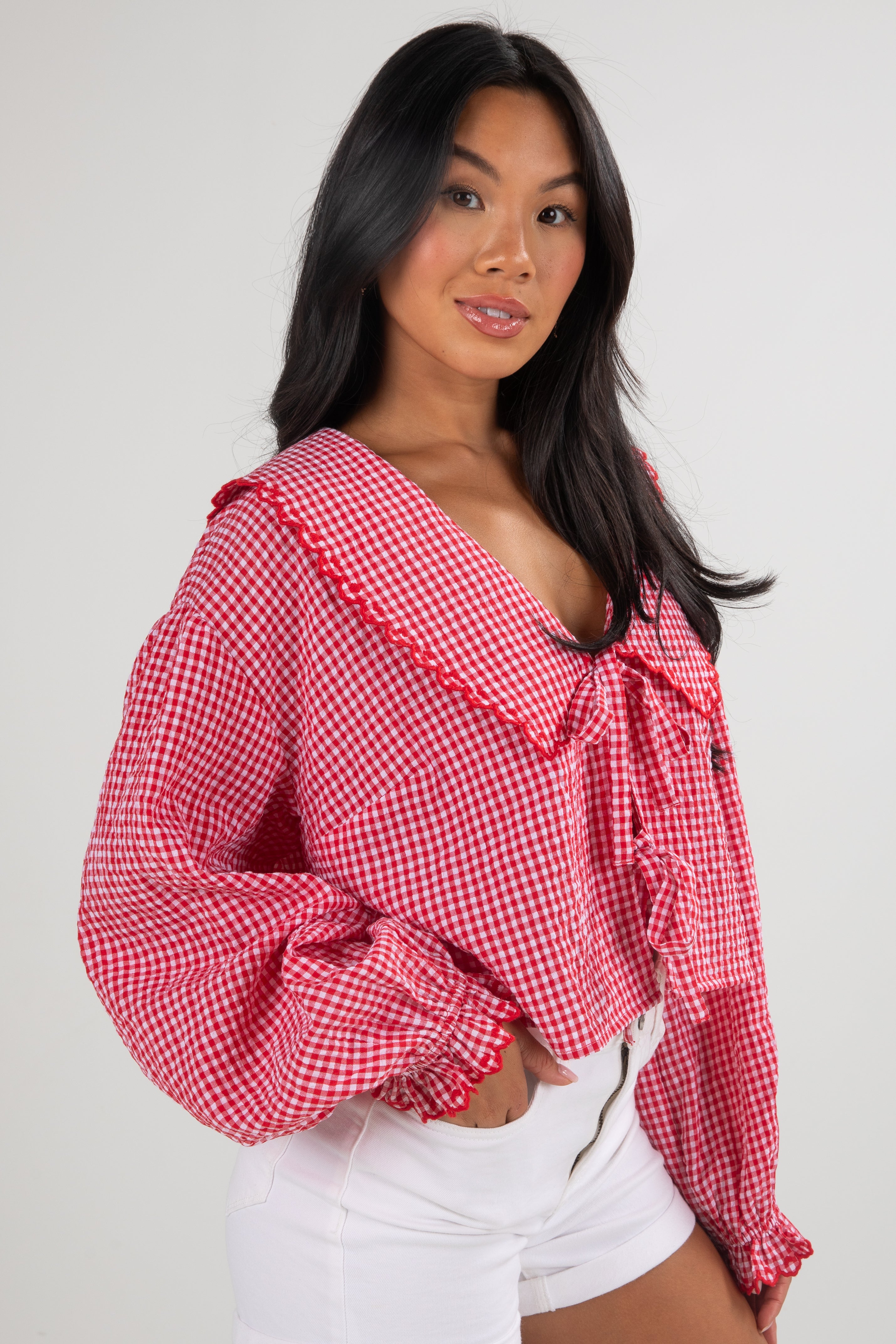 Woman wearing a red and white checkered blouse with ruffled sleeves on a plain background