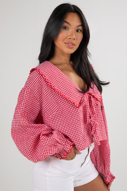 Woman wearing a red and white checkered blouse with ruffled sleeves on a plain background