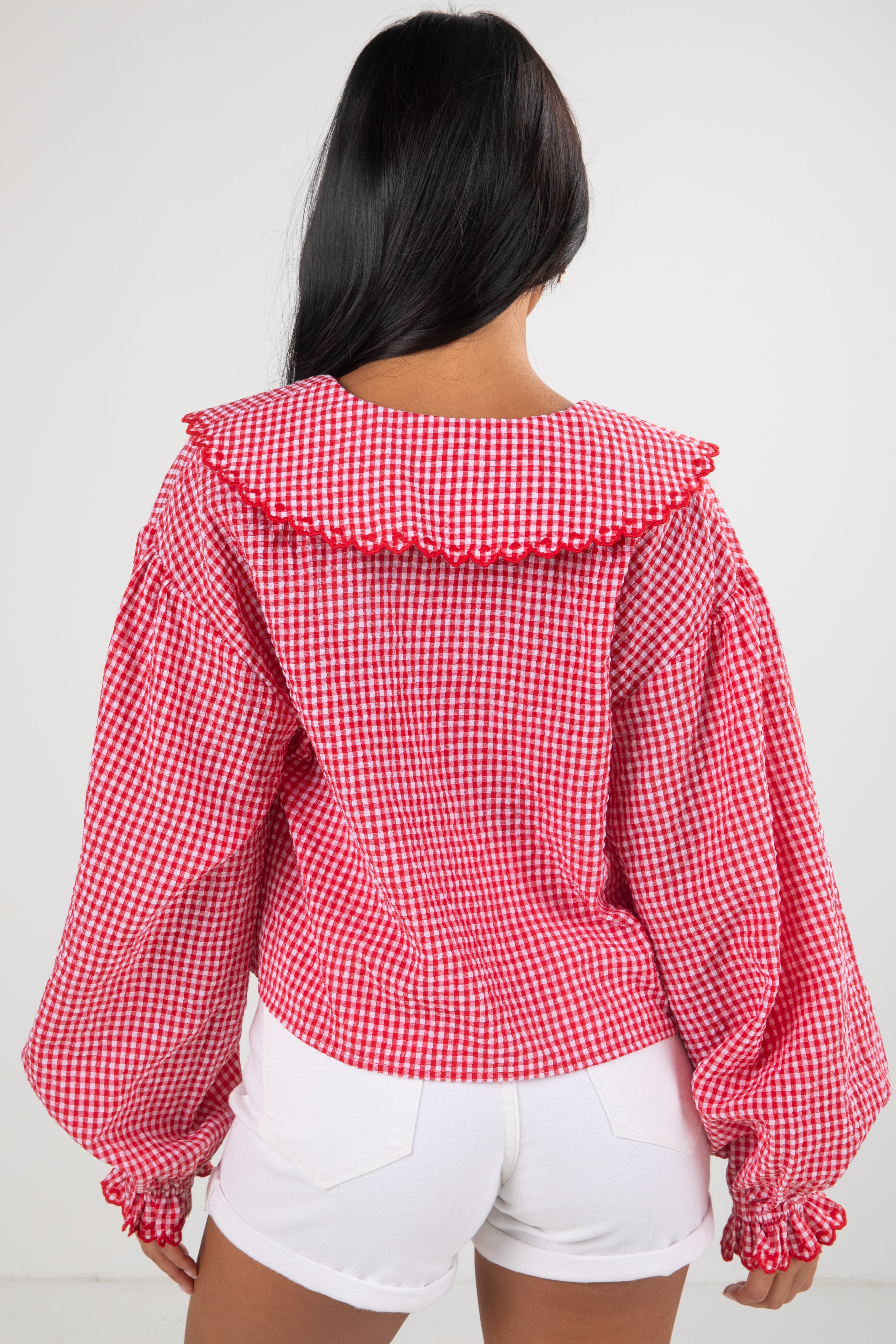 Person wearing a red and white checkered blouse with ruffled collar on a plain background