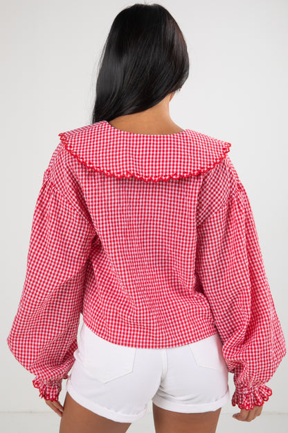 Person wearing a red and white checkered blouse with ruffled collar on a plain background