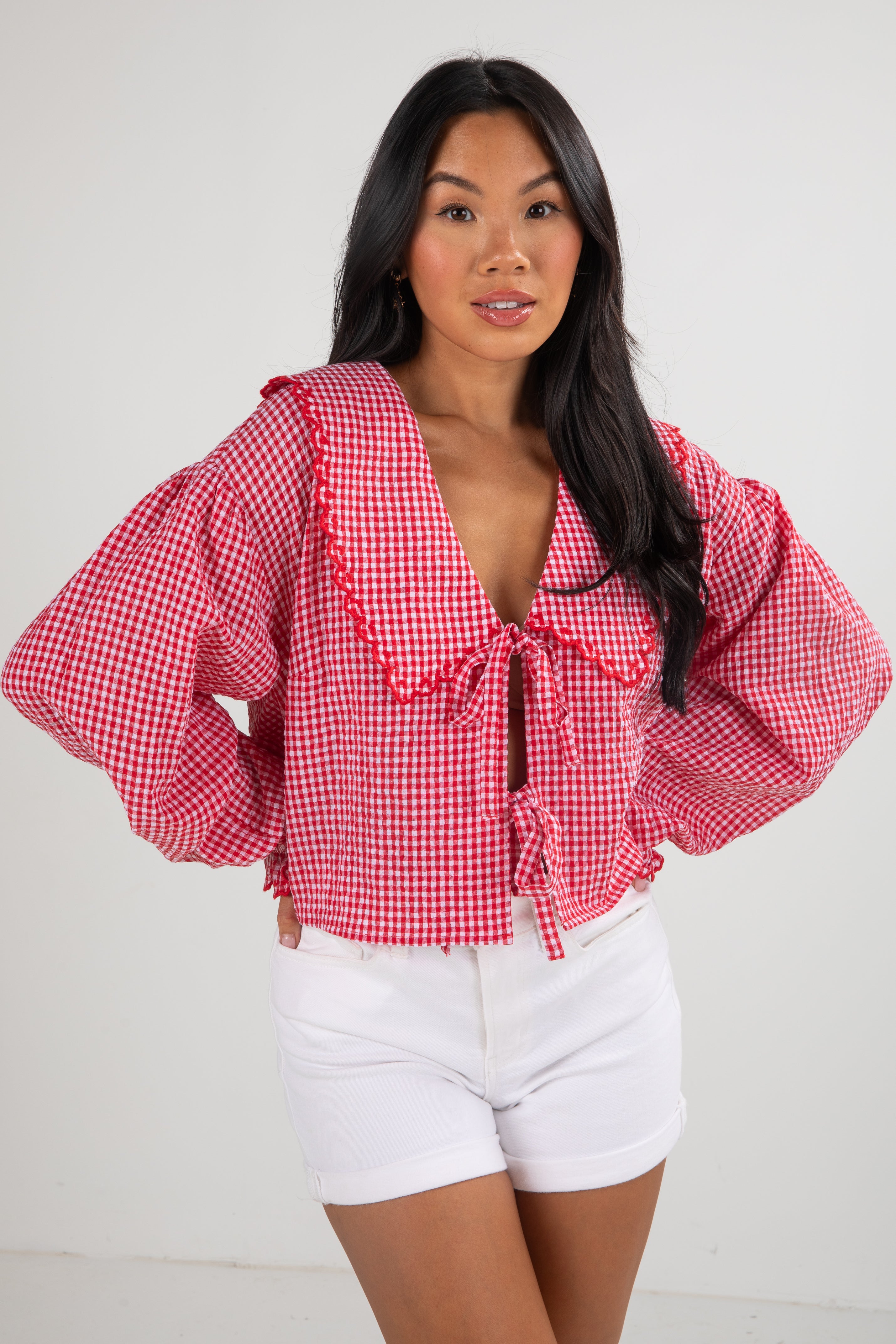 Woman wearing a red checkered blouse and white shorts on a plain background