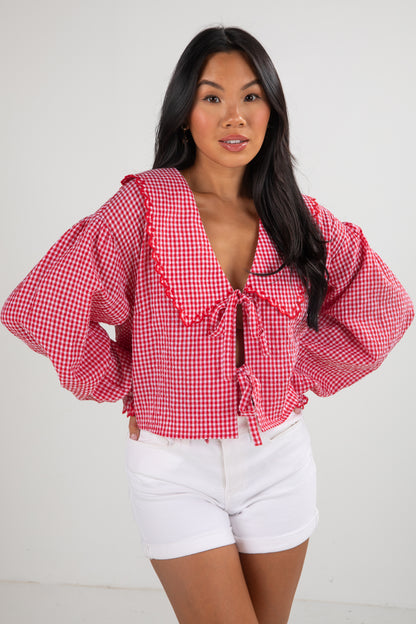 Woman wearing a red checkered blouse and white shorts on a plain background