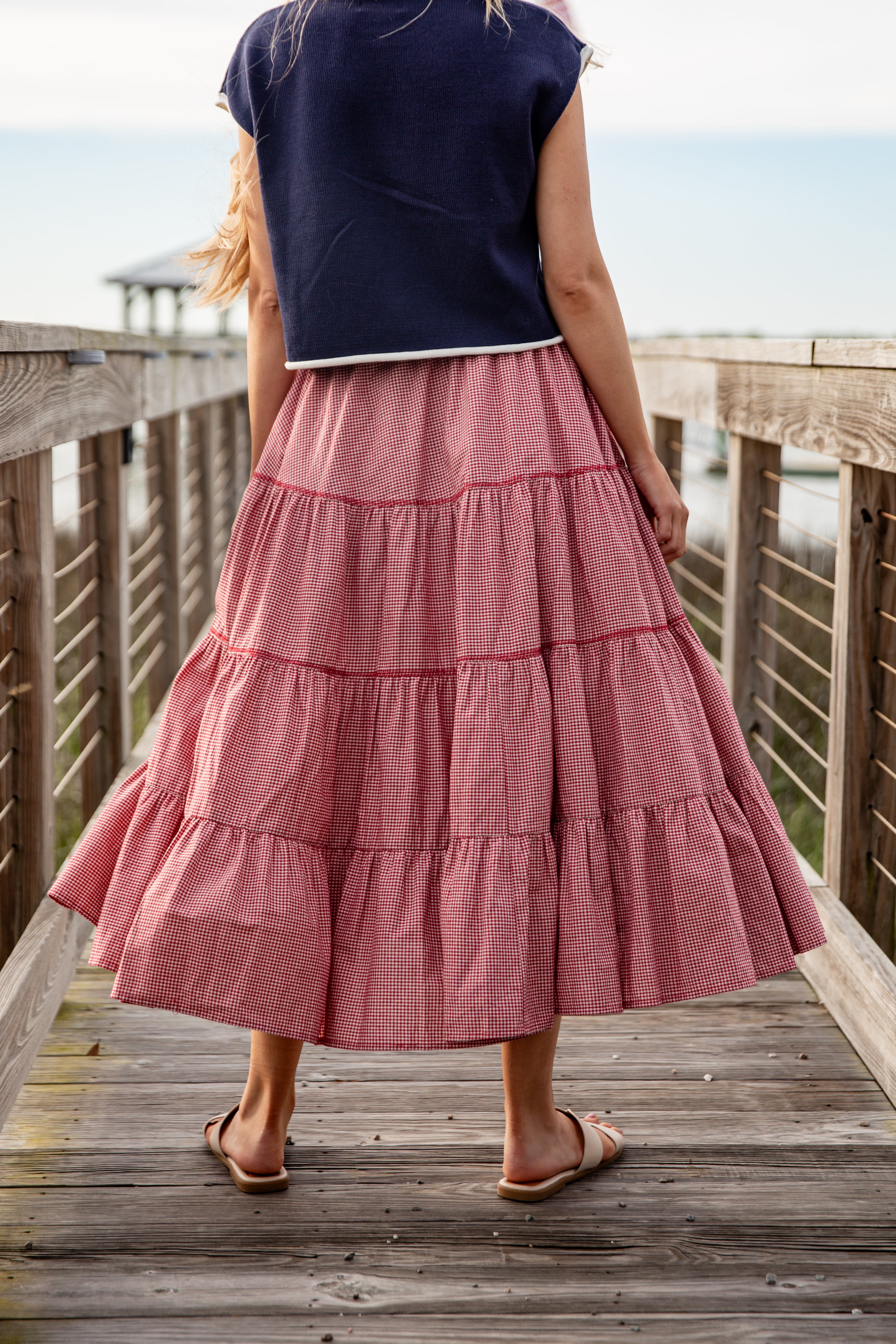 Person wearing a navy top and pink tiered skirt on a wooden deck by a waterfront.