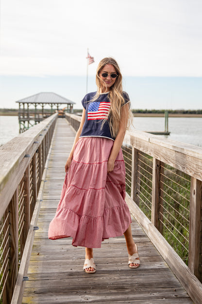 Woman in a pink dress and navy t-shirt with an American flag on a wooden dock.