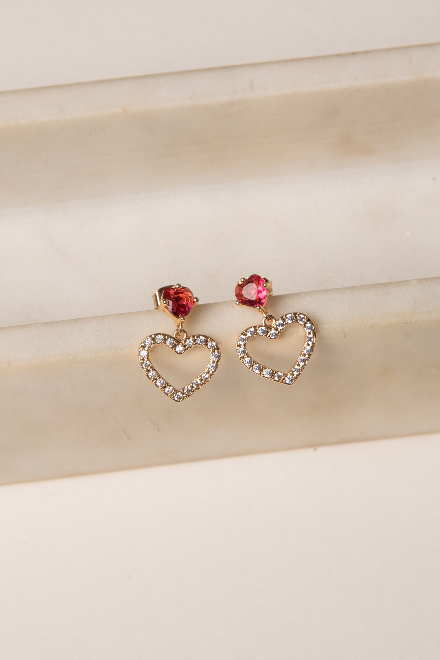Heart-shaped earrings with red gemstones on a beige fabric background