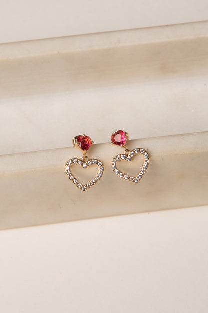 Heart-shaped earrings with red gemstones on a beige fabric background