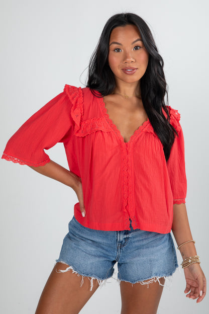 Woman wearing a red blouse with ruffled sleeves and denim shorts on a white background