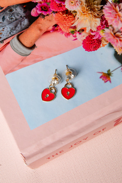 Heart-shaped earrings on a pink book with flowers in the background