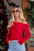 Woman wearing a red off-shoulder top and sunglasses in front of a decorated Christmas tree.