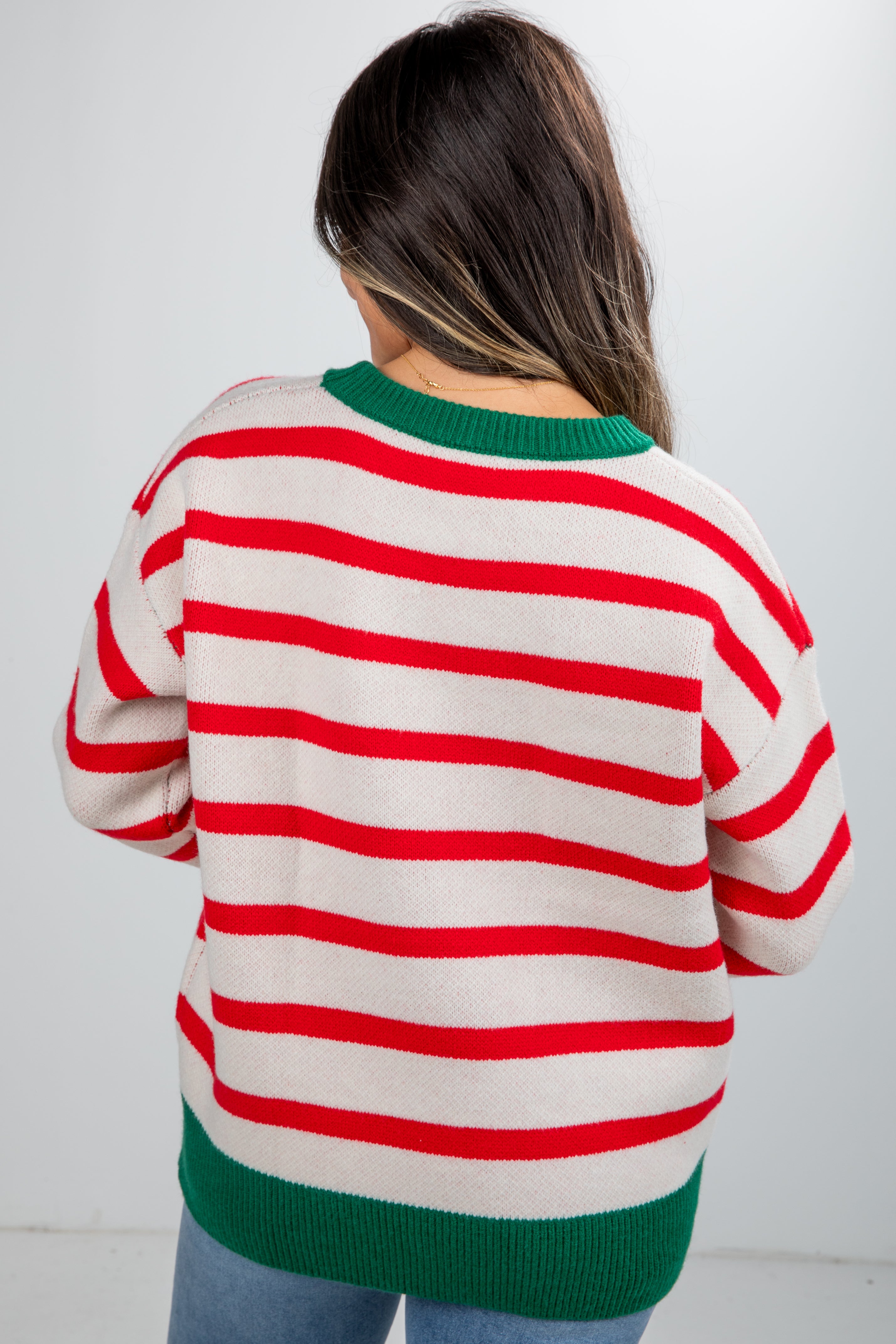 Person wearing a red and white striped sweater with green trim on a plain background