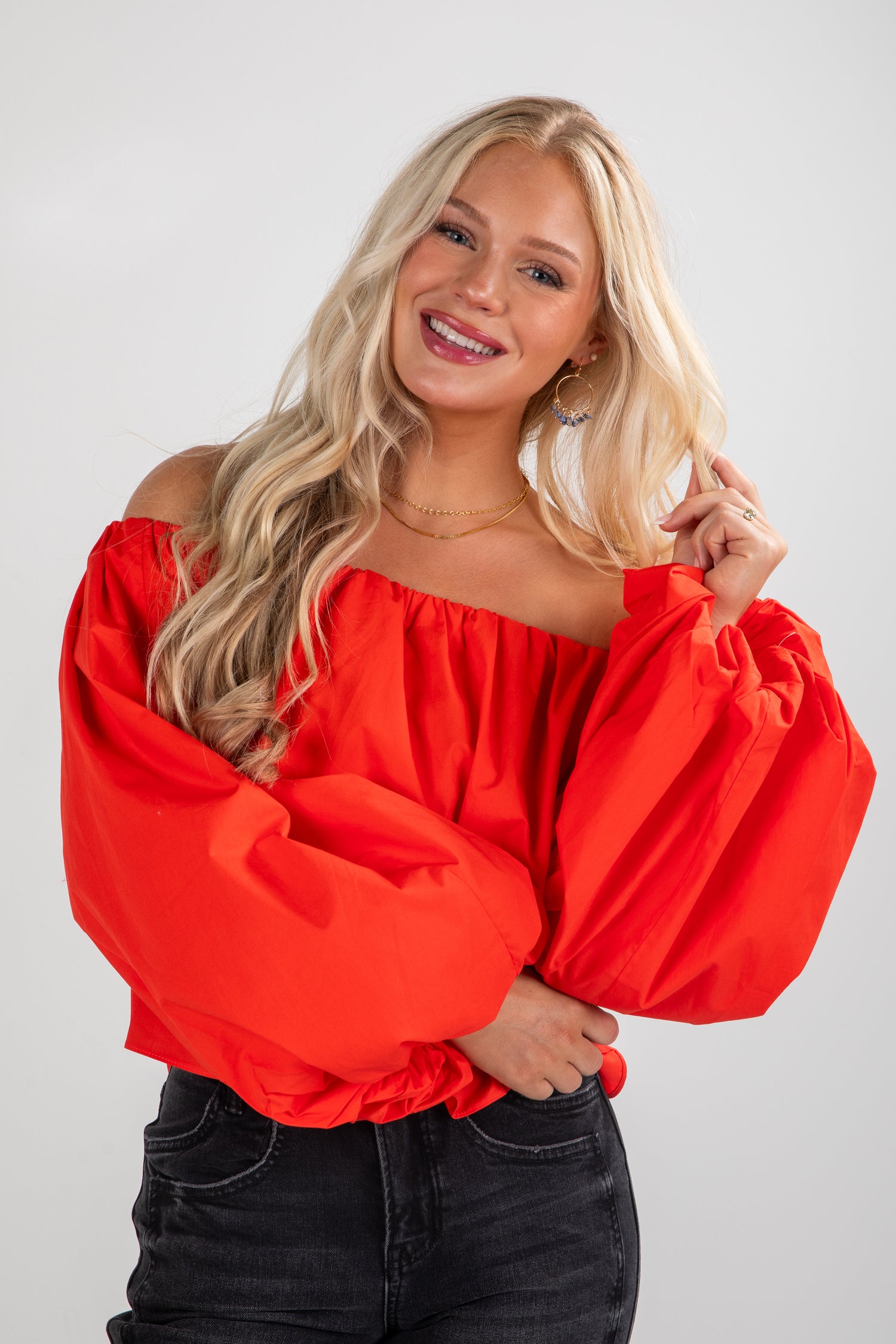 Woman wearing a bright red off-shoulder top against a plain background