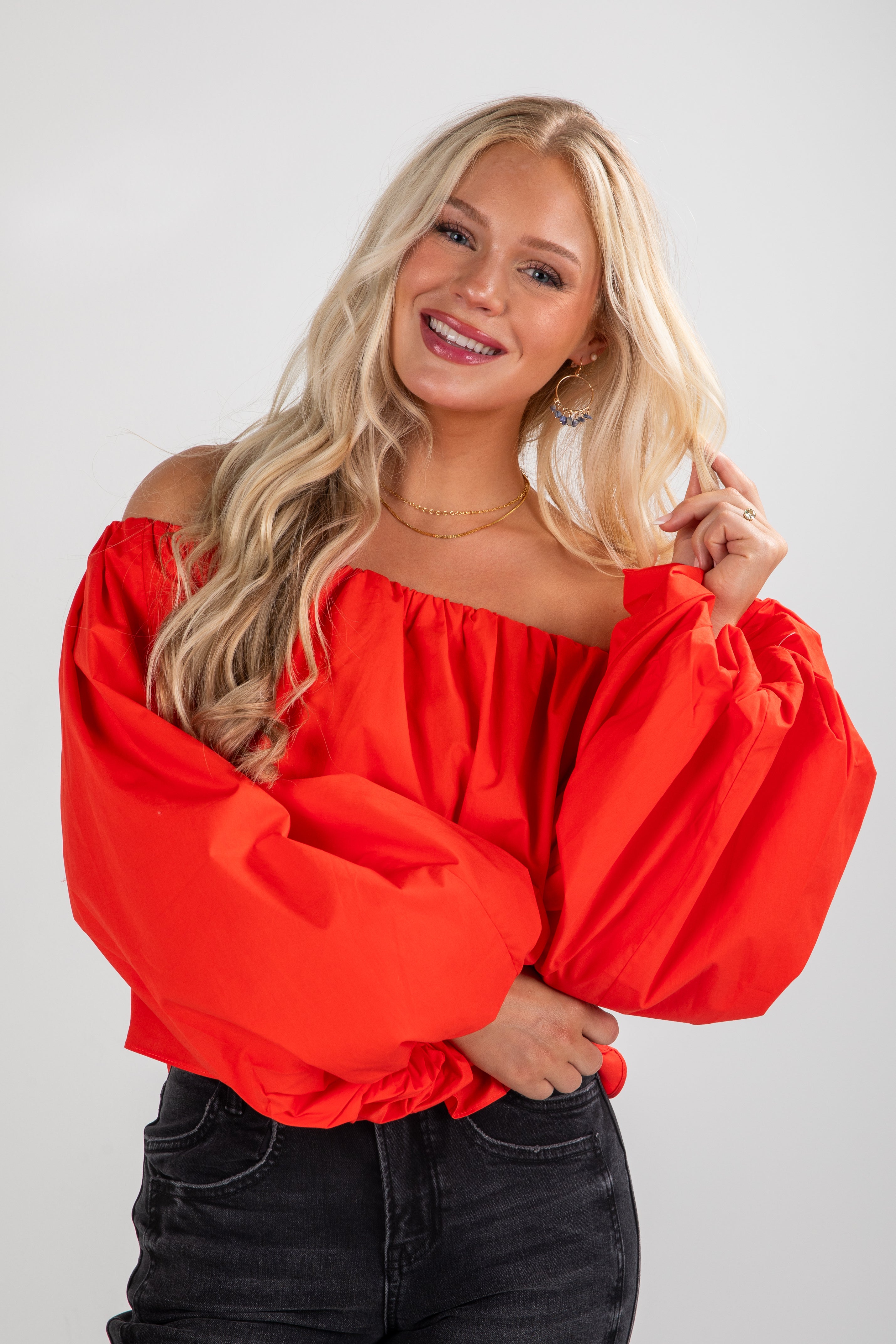 Woman wearing a bright red off-shoulder top against a plain background
