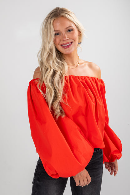 Woman wearing a red off-shoulder top against a white background
