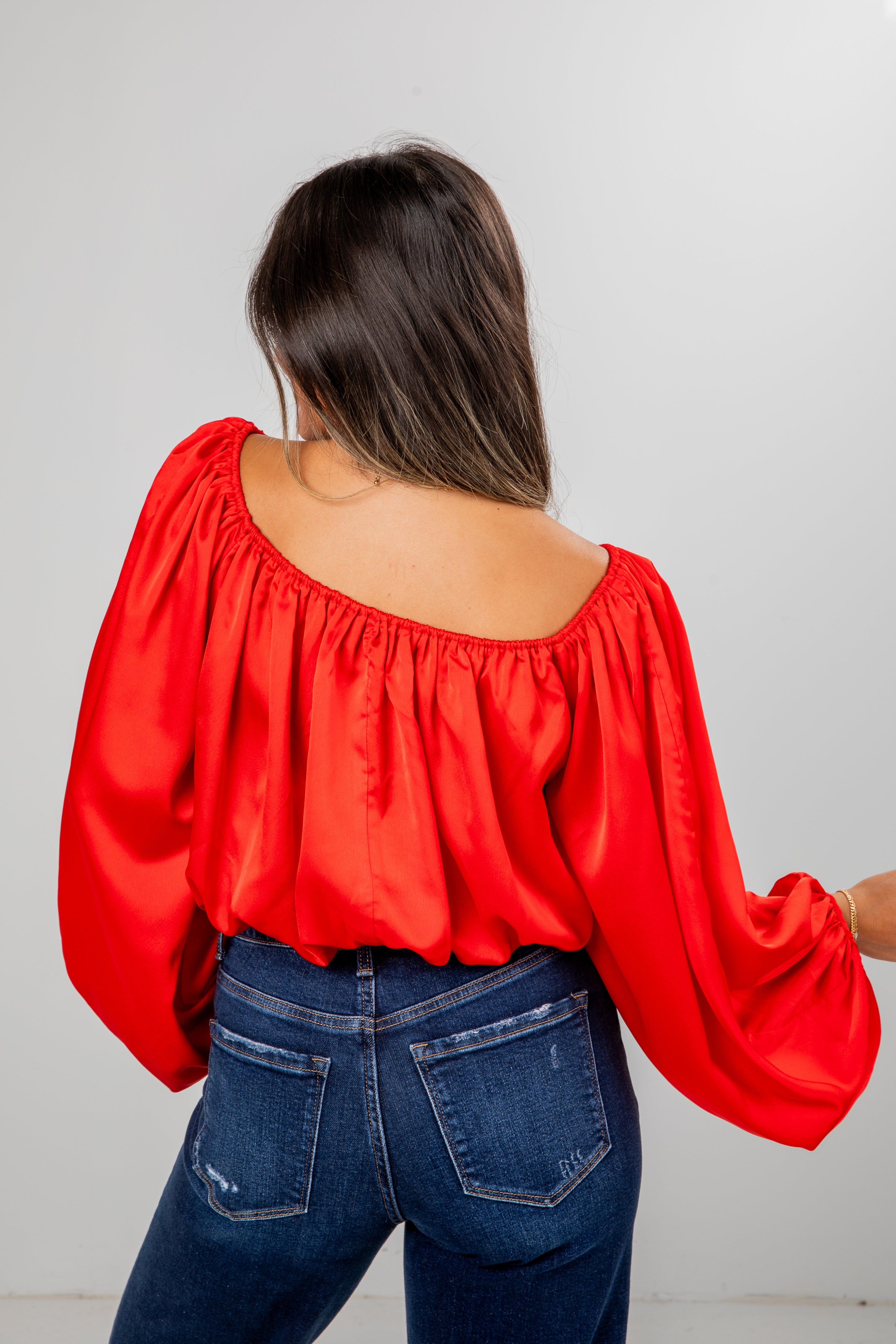 Woman wearing a red blouse with balloon sleeves and blue jeans on a plain background